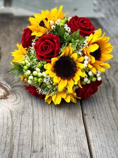 a bouquet of sunflowers and red roses on a wooden table with other flowers