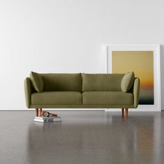 a green couch sitting in front of a painting on the wall next to a pair of shoes