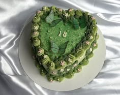 a heart shaped cake with green frosting and butterflies on it's top, sitting on a white plate