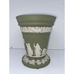 a large green vase with white designs on the sides and people painted on the side