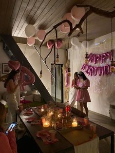 two women standing in front of a table with pink balloons and candles on the wall