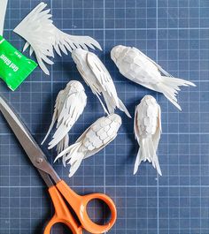 some white paper birds sitting on top of a blue table next to scissors and a tube of toothpaste