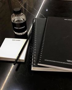 two notebooks and a pen are sitting on a table next to a bottle of water