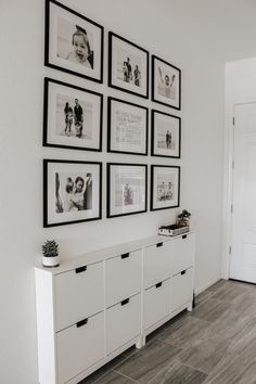 a white room with black and white pictures on the wall, drawers and cabinets in front of it