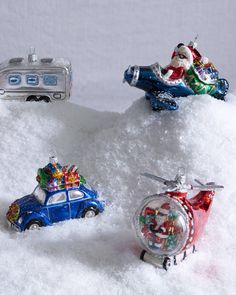 three christmas ornaments sitting on top of snow next to an alarm clock and toy car