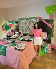 a woman standing in front of a table with pink and green items on it,