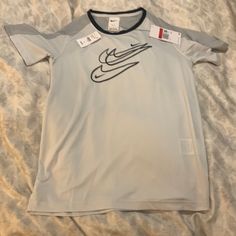 This Lightweight T-Shirt Is Light Gray With Dark Gray On The Shoulders. The Nike Swish Design Is In The Front. Gray Short Sleeve Sports Top, Nike Gray Sports T-shirt, Nike Gray T-shirt With Logo Print, Nike Gray Tops With Letter Print, Nike Sports T-shirt In Gray, Nike Gray Sports Top, Gray Nike Sports Top, Nike Moisture-wicking Crew Neck Tops, Graphic Tee With Crew Neck For Sports