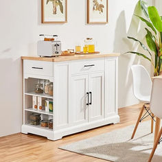 a small kitchen with white cabinets and wood flooring in the dining room, next to a potted plant