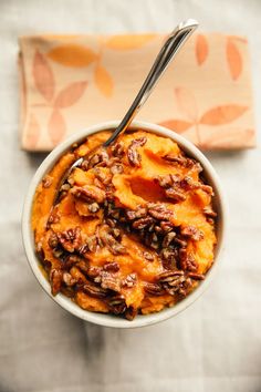 a white bowl filled with sweet potato casserole on top of a table next to a napkin