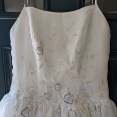 a white dress with flowers on it hanging from a hook in front of a door