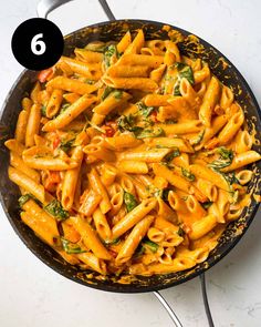 a skillet filled with pasta and spinach on top of a white countertop