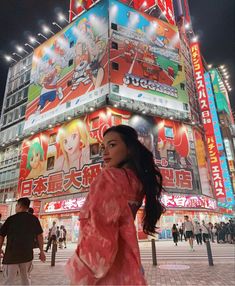 a woman walking in front of a tall building with advertisements on it's side