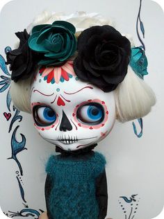 a doll with white hair and blue eyes wearing black roses in her hair is standing next to a wall