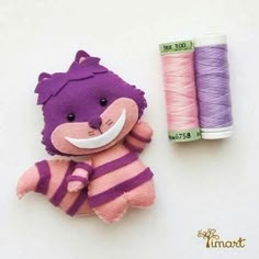 a purple and pink stuffed animal next to two spools of thread on a white surface