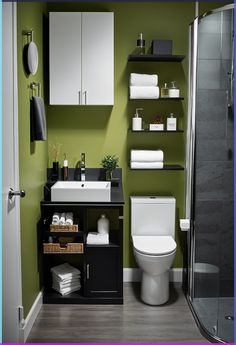 a small bathroom with green walls and white fixtures on the shelf above the toilet is a black cabinet