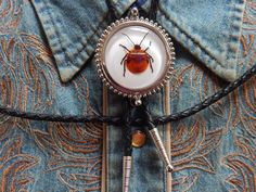 "We are a small independent company based in Derbyshire. We source our materials Worldwide to create something different and unique Our lovely Bolo ties are crafted/assembled by us in our workshop. This bolo tie has a genuine Flower bug set in clear resin . Every piece is crafted so there will be slight differences from the image in every one .  Silver colour metal trim and tips with a black leather cord standard length 36\" can be made shorter or longer if requested.Faux leather available.Sprin Flower Bolo Tie, Bolo Ties, Boho Men, Bolo Tie, Metal Trim, How To Make Shorts, Bugs And Insects, Clear Resin, All That Glitters