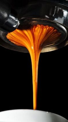 orange liquid pouring from a faucet into a white bowl on a black background