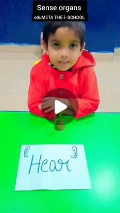 a little boy sitting at a table with a sign on it that says hear 3