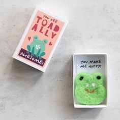 an open box with a small green frog in it next to a card that says you are too ally