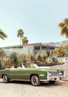 an old green car parked in front of a palm tree and modern house with mountains in the background