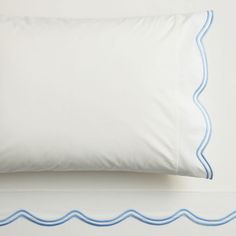 a white pillow with blue scalloped edges on a white bedding sheet set