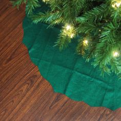 a close up of a green christmas tree skirt on a wooden floor with lights in the background