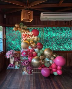 a birthday party with balloons and flowers in front of a large green wall that says happy birthday