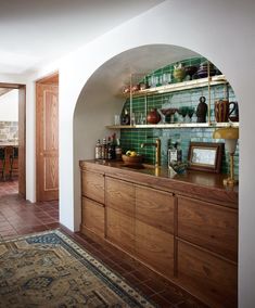 an arched doorway leads into a kitchen with green tile and wooden cabinetry, along with a rug on the floor