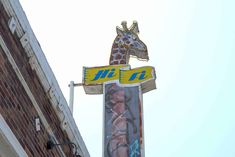 a tall giraffe sign hanging off the side of a building next to a brick wall