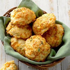 a basket filled with cheesy biscuits on top of a white wooden table next to a green napkin