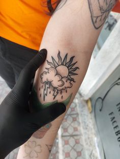 a person with a tattoo on their arm is holding onto a glove that has a sun and cloud tattooed on it