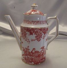 a red and white porcelain tea pot with a gold trimming on the top, sitting on a white tablecloth