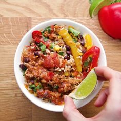 a person holding a spoon in a bowl filled with rice, beans, and veggies