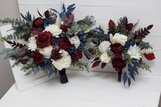 two bridal bouquets with red, white and blue flowers sit on a bench