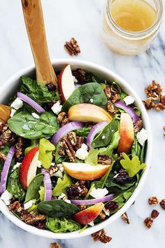 a salad with spinach, apples, walnuts and feta cheese in a white bowl