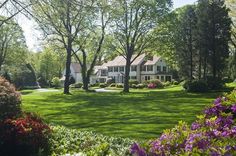 a large white house surrounded by trees and flowers