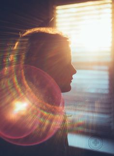 a person standing in front of a window with the sun shining down on her face