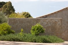 an old building is next to some bushes and trees on the side of the road