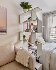 a living room with a couch and a book shelf next to a bed in front of a window