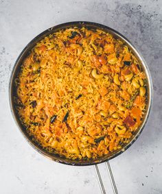 a skillet filled with pasta and vegetables on top of a white counter next to a spoon