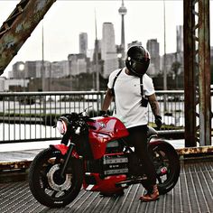 a man sitting on top of a red motorcycle next to a metal structure with a city skyline in the background