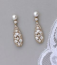 two pairs of pearl and crystal earrings on top of a white lace doily next to a lacy net