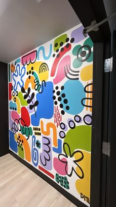 a large colorful painting on the side of a wall in an empty room with hard wood flooring