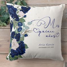 a white pillow with blue flowers and greenery on the front, against a wooden background