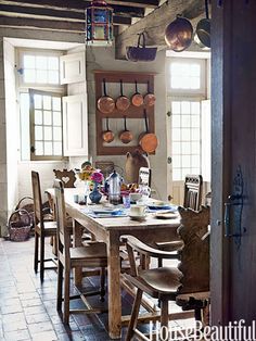 a dining room table with chairs and pots hanging from the ceiling in front of windows