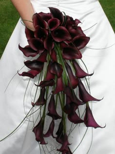 a bride holding a bouquet of purple flowers in her wedding dress with grass behind it