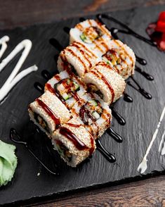 some kind of sushi on a black plate with sauce and garnishes