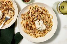 two plates of pasta with meat and vegetables on them next to a glass of green juice