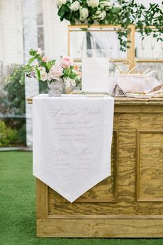 an elegant wedding reception with white linens and greenery on the side of a wooden cabinet