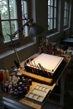 an artist's studio table with art supplies on it and a lamp in the background